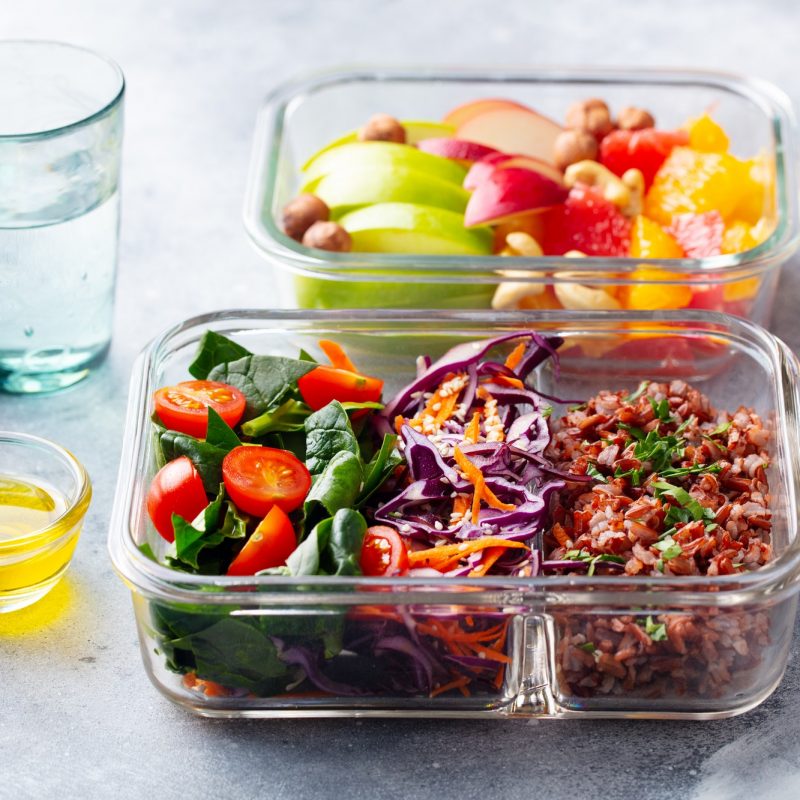 Lunch Box with Vegetables, brown rice and fruits salad. Healthy eating. Grey background.