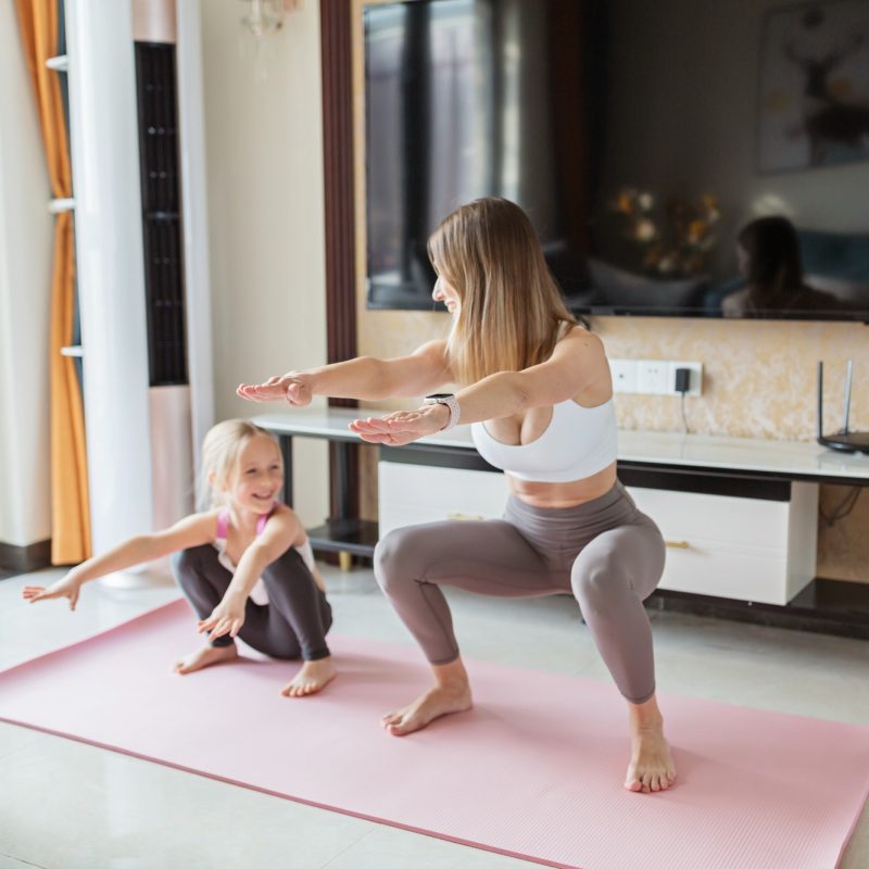 Young mother in sport clothing exercising at home with daughter. Online training during coronavirus